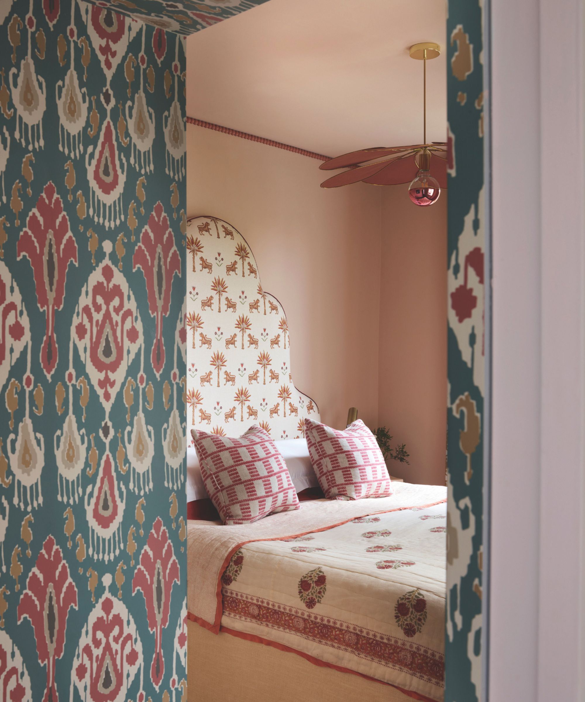 A master bedroom with pale pinks walls and heavily patterned bedding and blue patterned wallpaper
