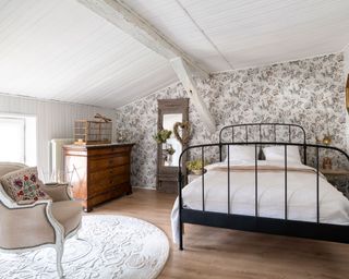 white bedroom with floral wallpaper, white pannelled walls and iron bed frame