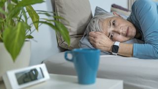 woman struggling to sleep with coffee cup by bed