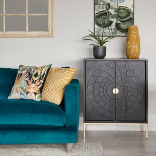 Blue velvet sofa with cushions, black cabinet, houseplants