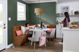 two daughters and a mother eat breakfast in their kitchen with a green accent wall