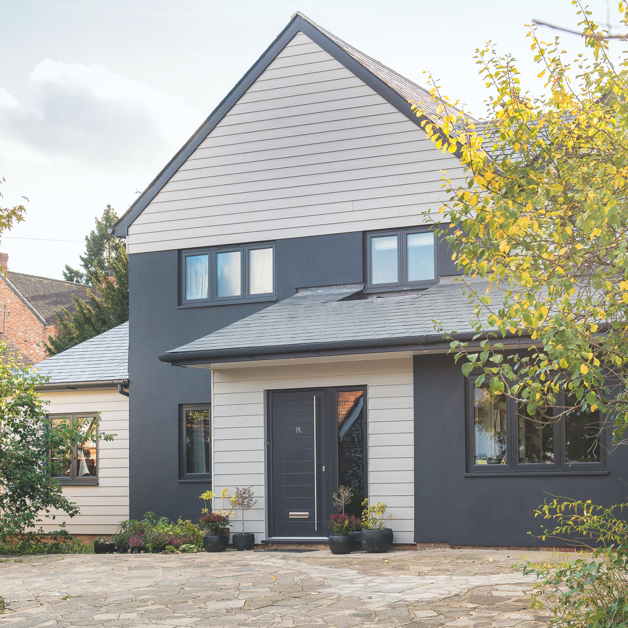 driveway leading to an extended house with dark grey render and white cladding