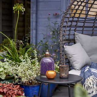 Garden egg chair with a table and decorations in front of it, surrounded by plants