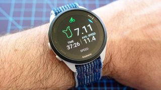 The Garmin Forerunner 165 GPS watch on a user's wrist with a blue woven band attached