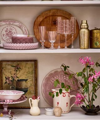 Pink wine glasses, jugs, cocktail shaker, pink plates and flowers all in a wooden dresser