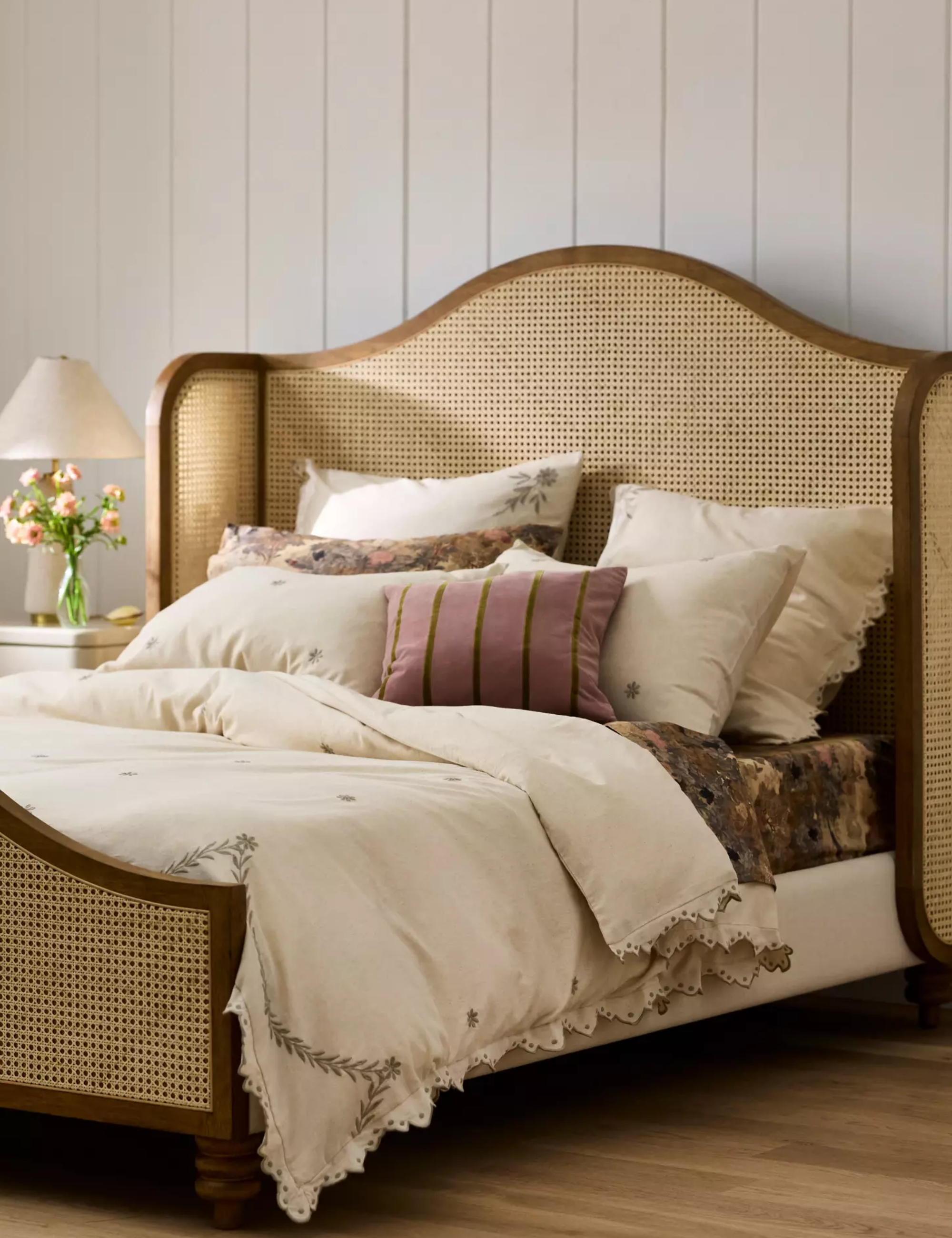 Grandma chic bedroom styled with floral-embroidered bed linens and a vintage cane bed frame
