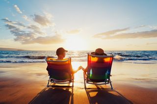 A couple relaxes in their beach chairs in front of a sunset