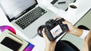 Beste gratis bilderedigeringsprogram: En person som holder et speilreflekskamera med en laptop i bakgrunnen