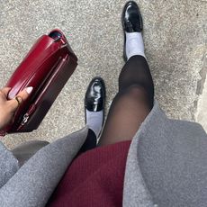 Lauren Tappan modeling fall work shoes, wearing loafers, a gray coat, a red dress, and a red bag