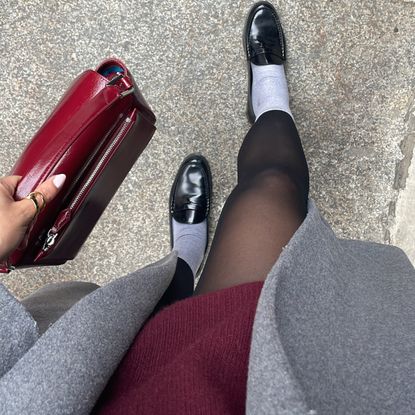 Lauren Tappan modeling fall work shoes, wearing loafers, a gray coat, a red dress, and a red bag 