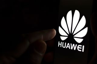 A finger about to press a Huawei logo in a dark room