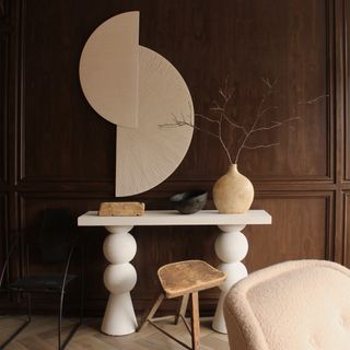 A living space with wood effect panelled walls, a white side table, and a wooden stool