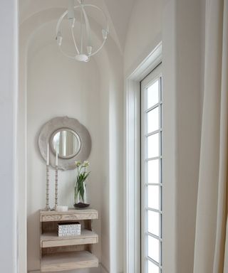 Light beige entryway space with round wall mirror atop console and white sculptural pendent lighting