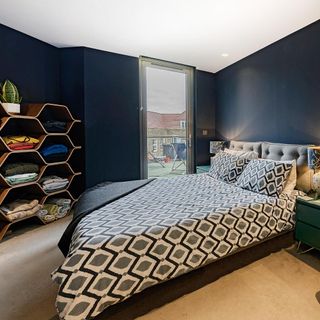 Bedroom with navy blue walls and bed with bold geometric bedding and freestanding shelves
