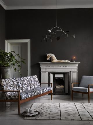 A black living room with black walls and a monochrome mid century sofa and ornate fireplace