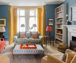 Blue living room with yellow curtains and an upholstered ottoman coffee table in Christopher Farr Cloth fabric