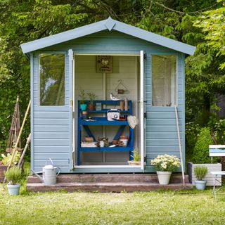 shed painted blue with dark blue potting table inside and chairs outside