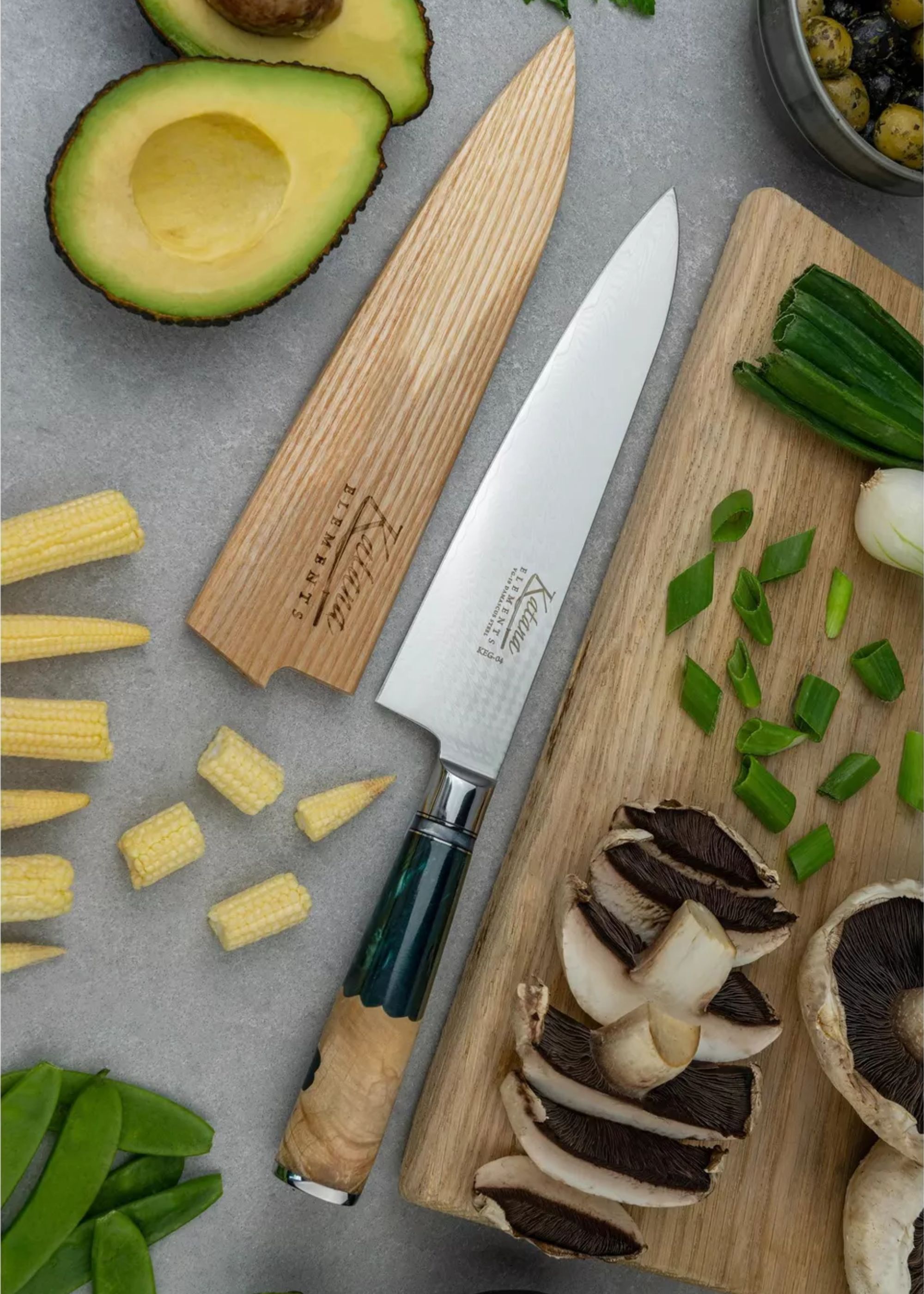 A Japanese knife beside a wood sheath and a chopping board with chopped mushrooms, baby corn, chives, and avocado