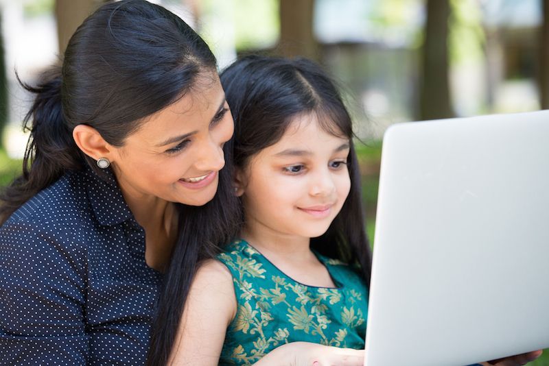 A mom and her daughter look at a laptop screen together.