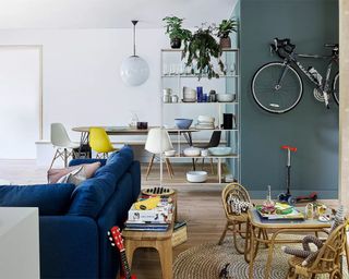 An open plan living room by John Lewis with blue velvet sofa, round dining room, modular shelves and play area