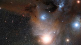 Cloudy, hazy and glowing structures are seen against a star-spotted background of space.