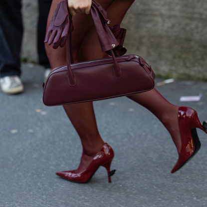 PARIS, FRANCE - MARCH 06: Tiffany Hsu wears red tights, Magda Butrym burgundy bag, grey belted overall outside Rick Owens during the Womenswear Fall/Winter 2025/2026 as part of Paris Fashion Week on March 06, 2025 in Paris, France. (Photo by Christian Vierig/Getty Images)