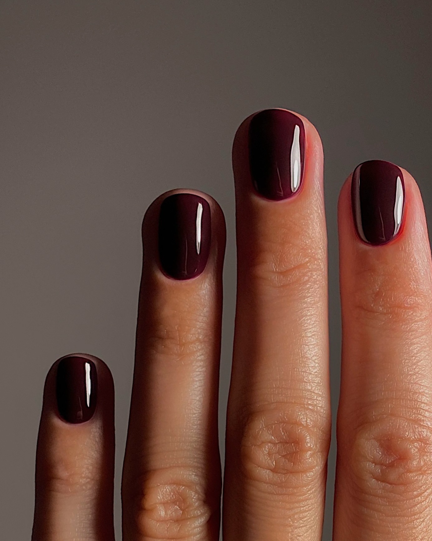 Short, rounded nails painted in a glossy deep plum-burgundy polish