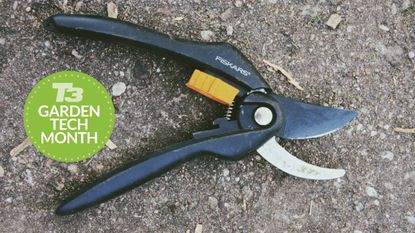 A pair of secateurs lying on dirty ground with a T3 Garden Tech month badge