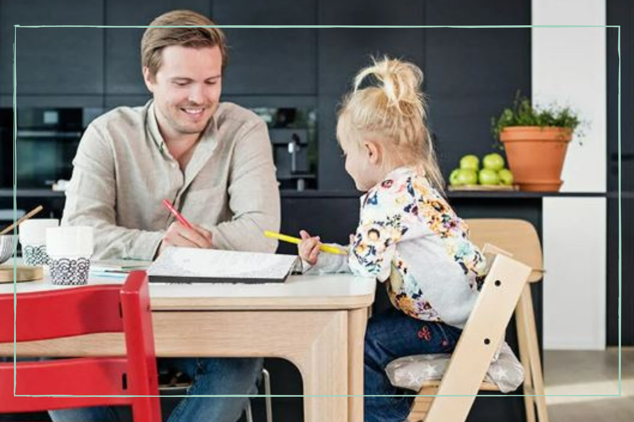 A little girl sits in a Stokke Tripp Trapp high chair at the table with her father