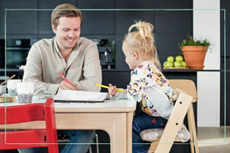 A little girl sits in a Stokke Tripp Trapp high chair at the table with her father