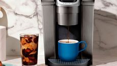 Keurig K-Elite Single Serve coffee maker with prepared hot coffee in blue mug and iced coffee in glass tumbler