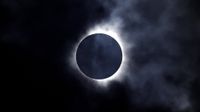 a murky total solar eclipse with part of the corona visible through dramatic clouds.