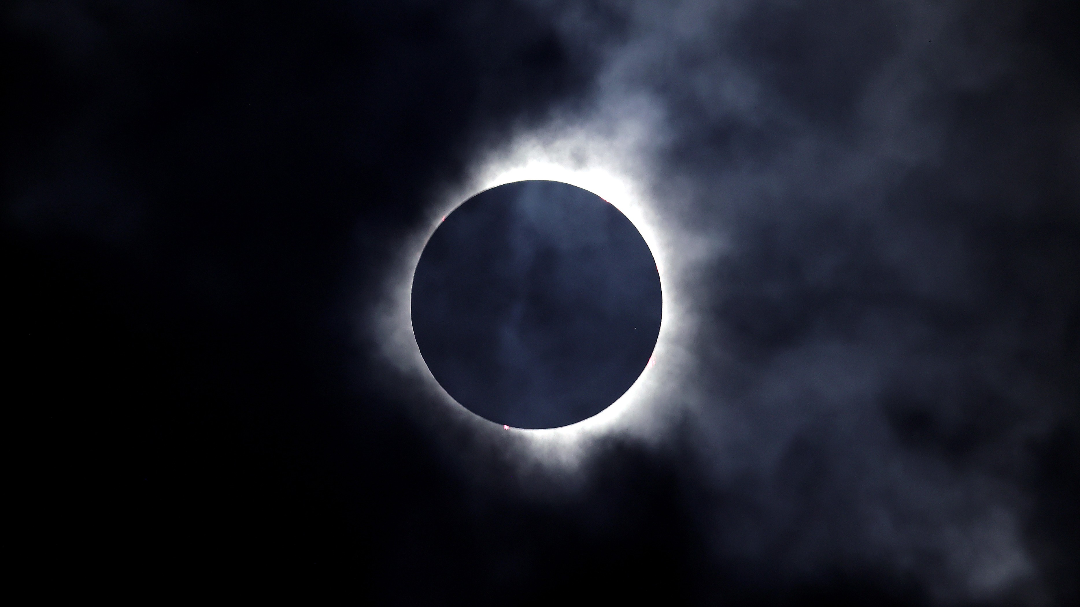 a murky total solar eclipse with part of the corona visible through dramatic clouds.
