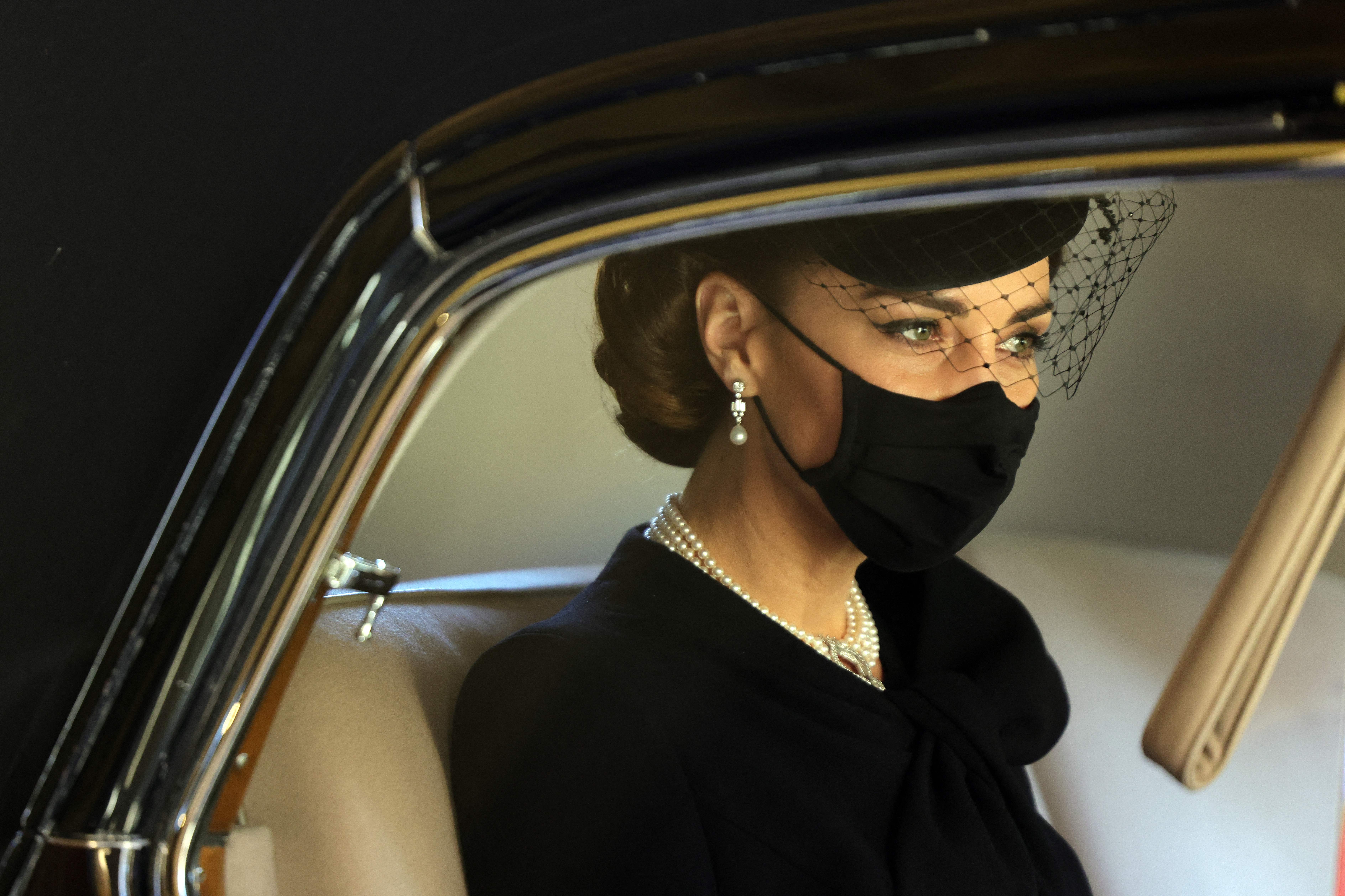 Princess Kate wearing a black outfit and mask in a car