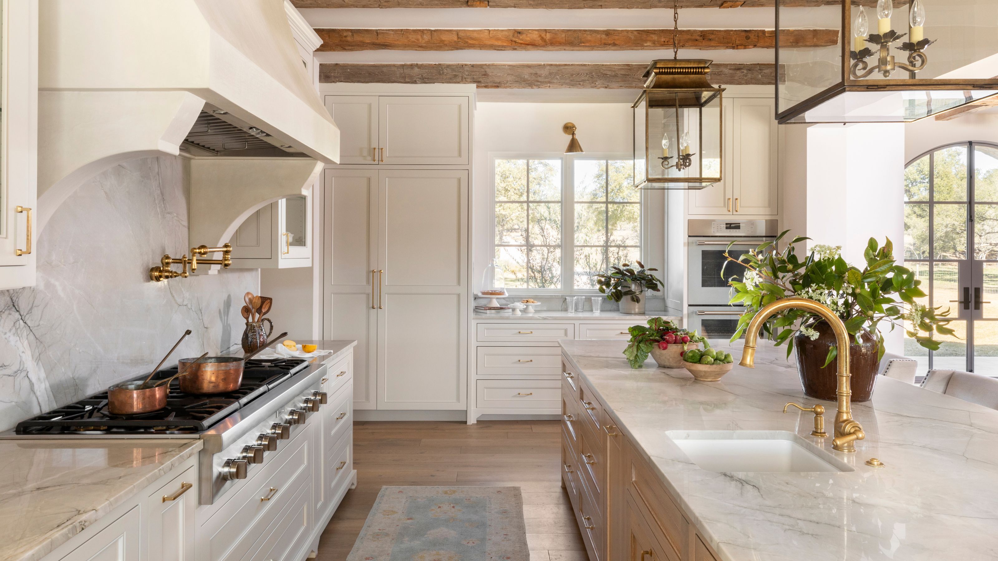 a farmhouse white kitchen with vintage style range cooker and hood with an oak island with a sink and marble counters