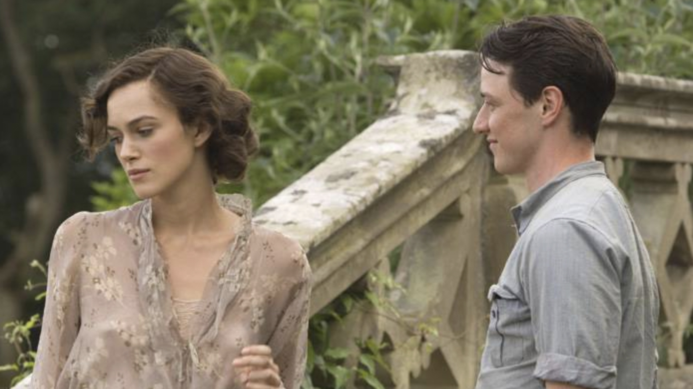 A still from the movie Atonement in which Keira Knightley's character Cecilia Tallis is wearing a pale pink dress and looking away from James McAvoy's character Robbie Turner