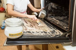 A close up of a woman spreading baking soda on an oven door