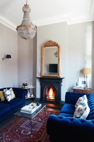 An elegant living room with two blue sofas and trad red rug, chandelier and brass-framed mirror