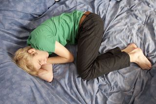 Blond teen boy lying in bed sad.