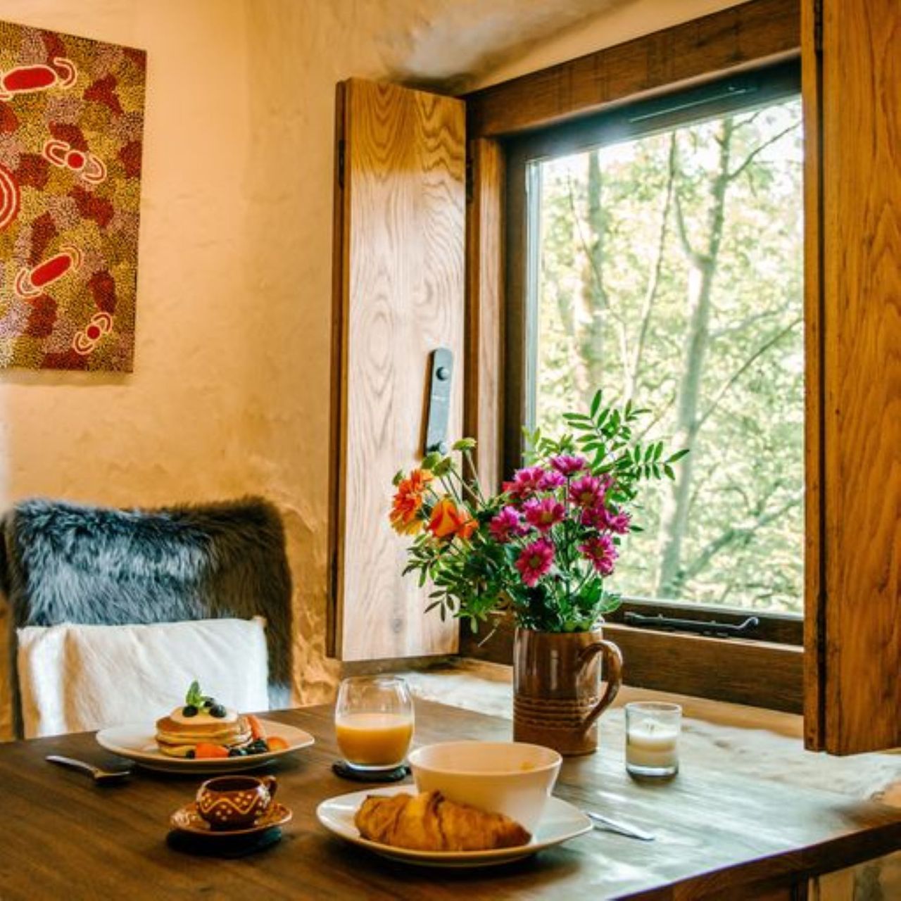 Two sitting places facing the wooden window with a flower vase on table overlooking the surrounding forestry