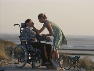 a woman in a green dress by the beach touches her hand to the cheek of a man in a wheelchair in The Diving Bell and the Butterfly