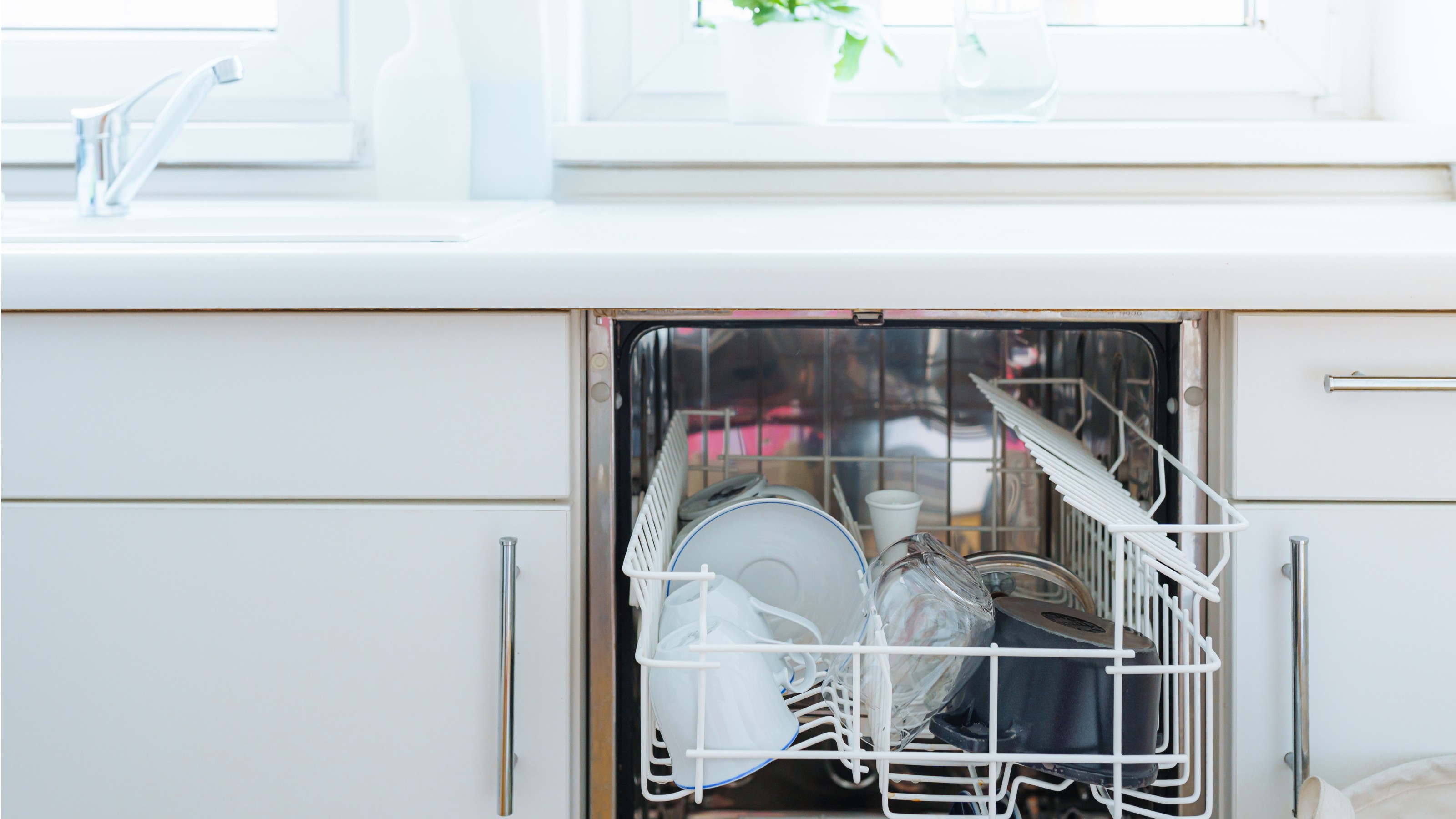 Integrated dishwasher with open door and neatly stacked crockery in white kitchen