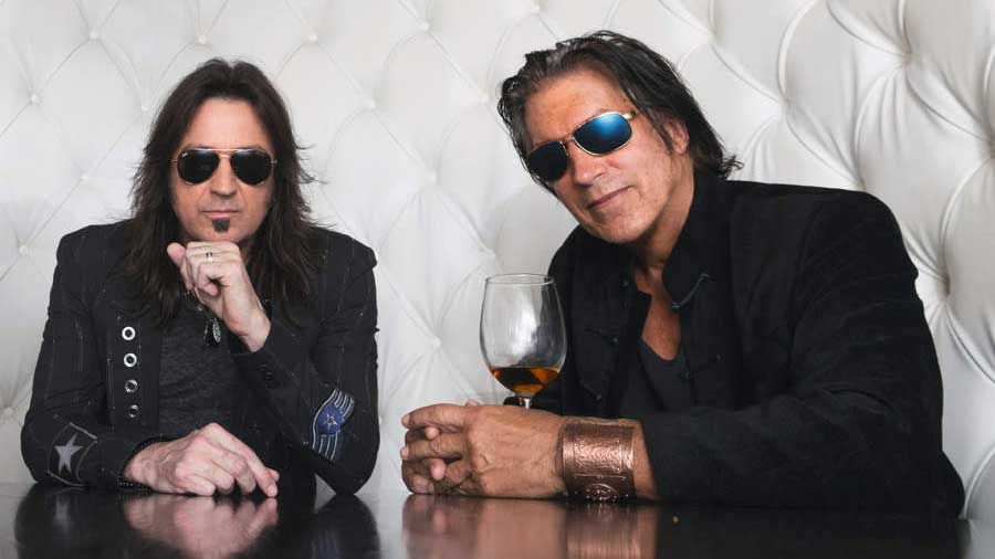 Sweet &amp; Lynch seated at a table wearing sunglasses