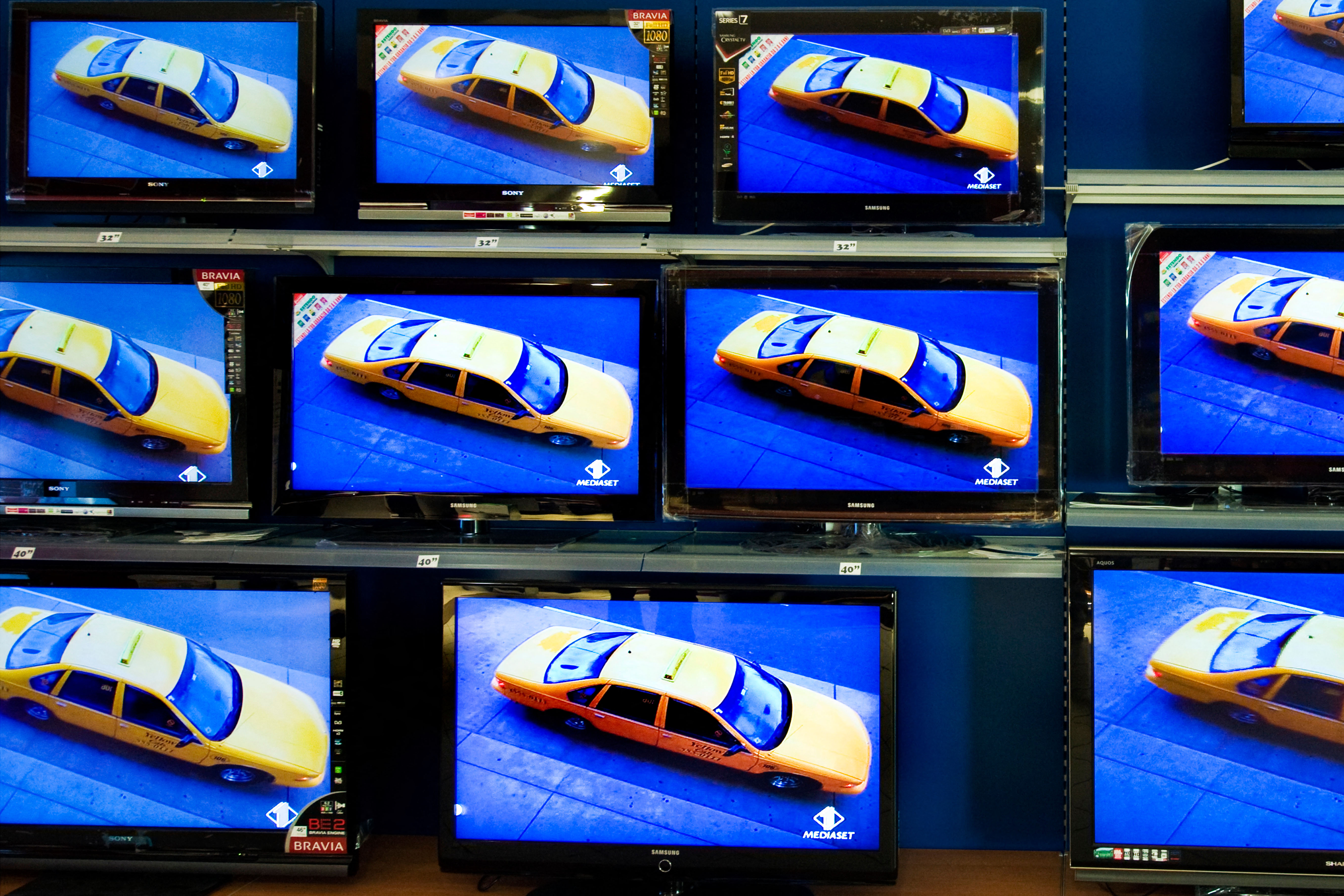 A row of vintage televisions, all showing the same picture, which is a yellow new york taxi