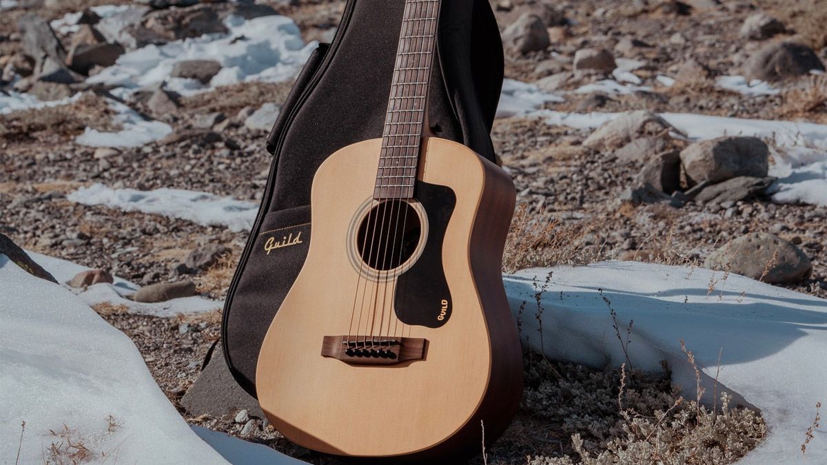 The Guild Travel Spruce acoustic is photographed on the side of a snow-covered hill-top, leaning against its gig-bag.