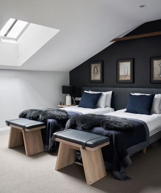 Black and white bedroom with twin beds, black painted feature wall, matching wooden stools, skylight