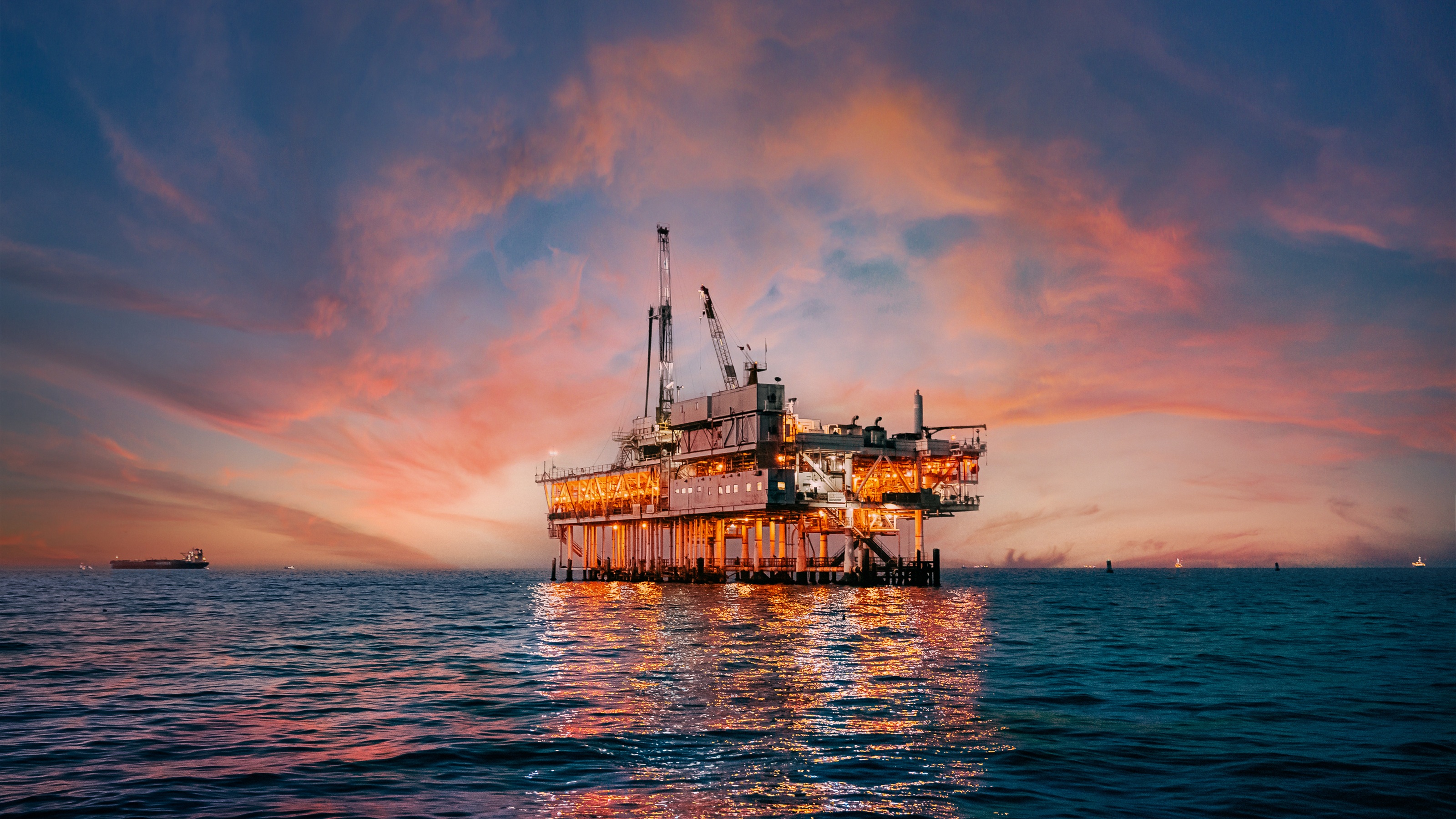 An oil rig in the ocean at sunset.