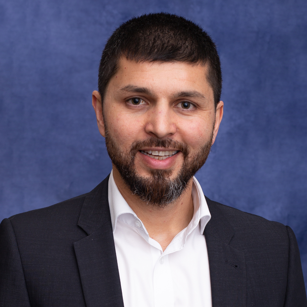 headshot of male with short dark hair,  beard, moustache wearing white shirt and dark suit jacket