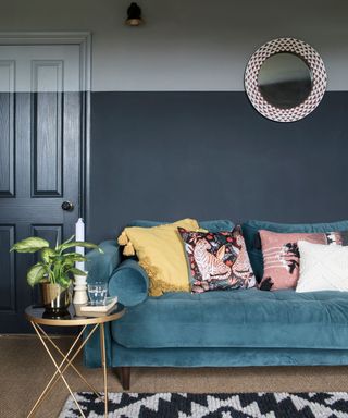 two tone dark grey blue living room with dark door, blue couch with pink yellow and white cushions and a small gold coffee table