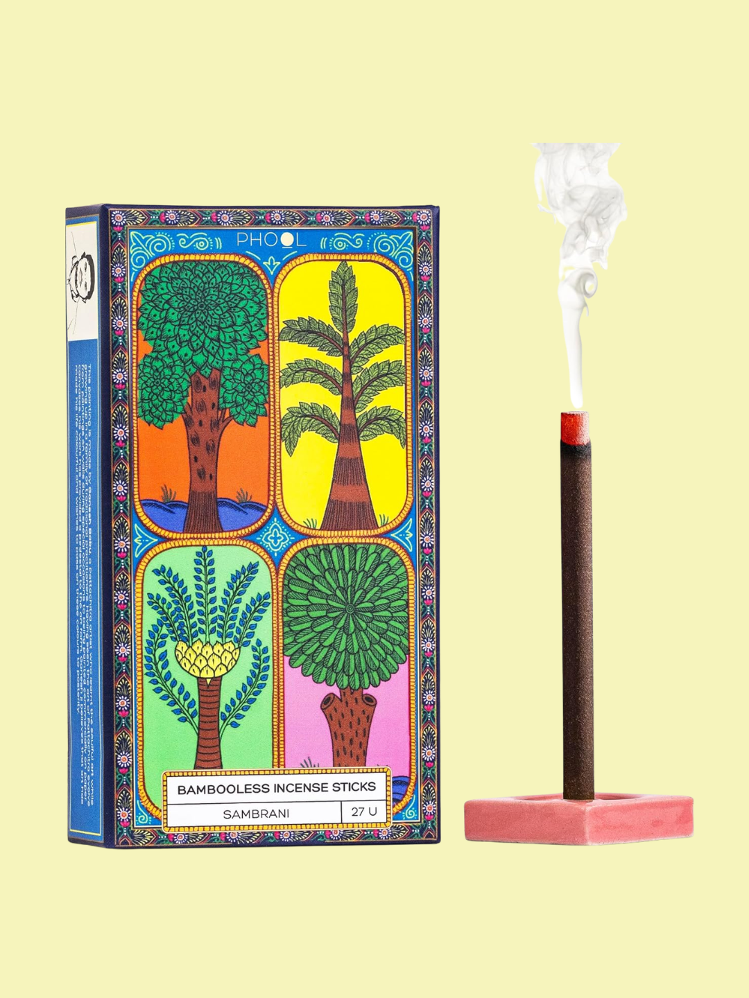 An incense stick on a pink holder beside a colorful patterned box from PHOOL
